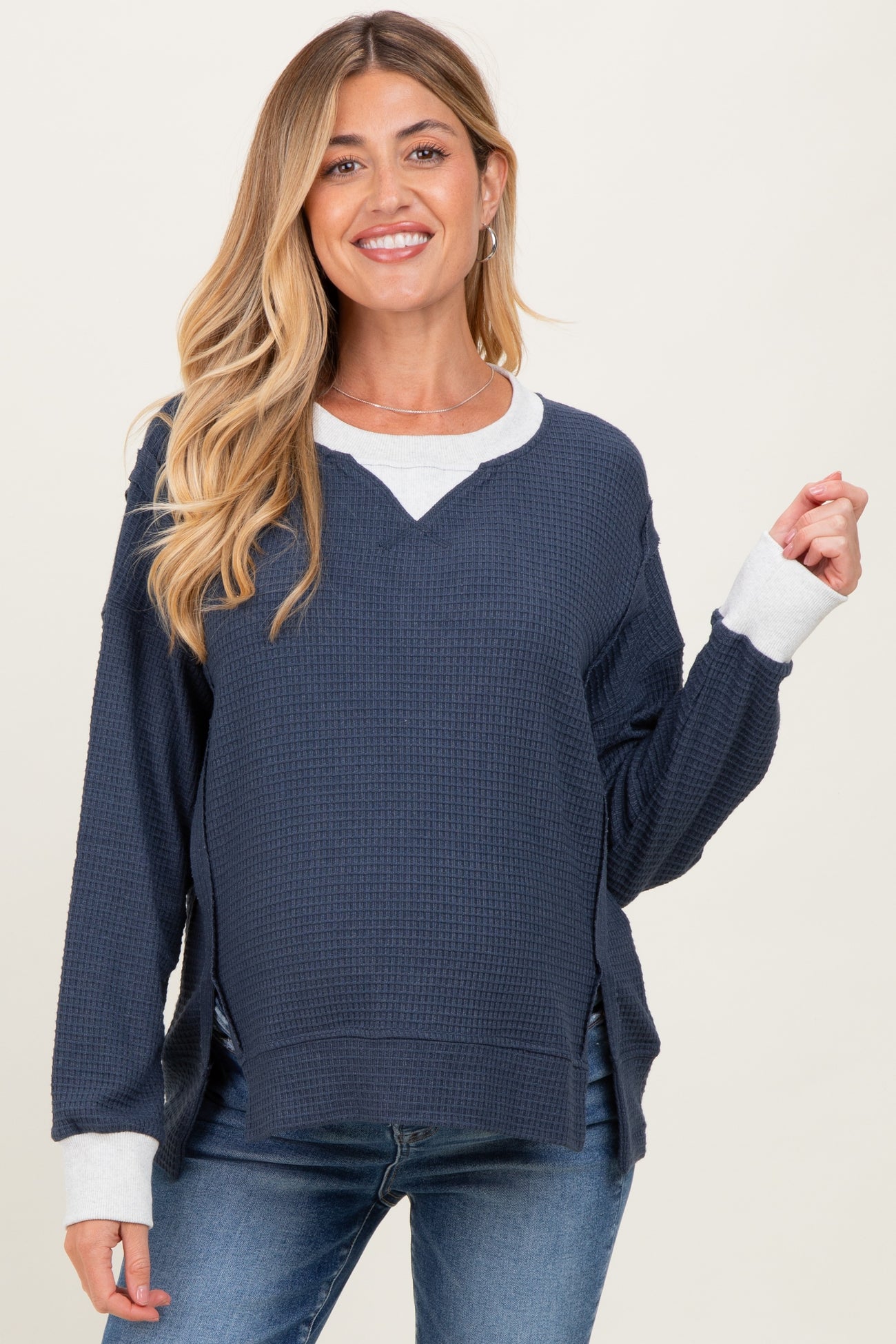 woman wearing a navy blue waffle knit maternity top with light gray trim and side slits, smiling at the camera