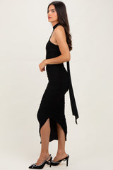 woman wearing a black halter neck ruched midi dress with side slits and a tie detail, styled with black heels