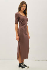 woman wearing a brown fitted midi dress with short sleeves and side slit, paired with black Converse sneakers