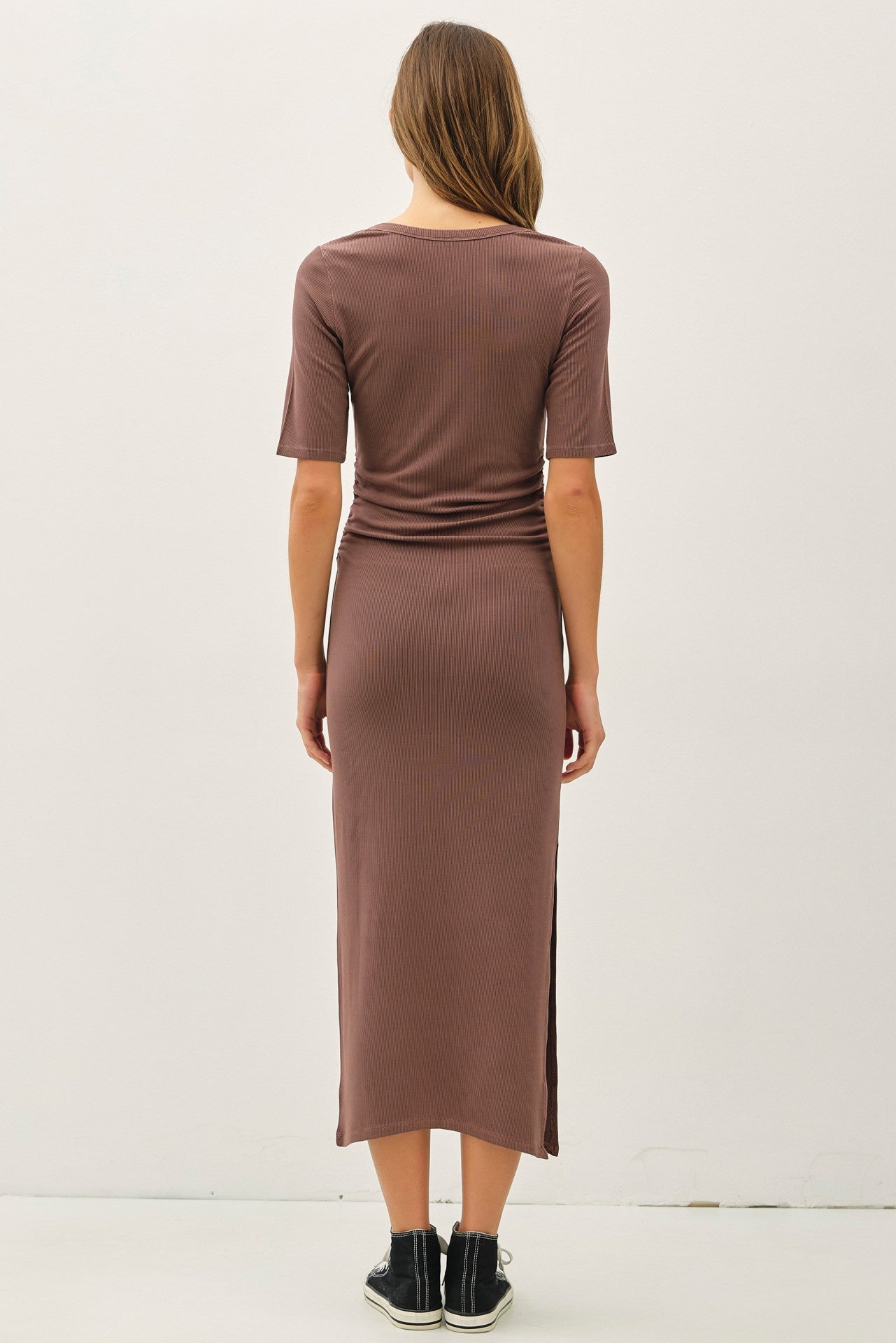 woman wearing a taupe fitted midi dress with short sleeves and side slits, seen from the back