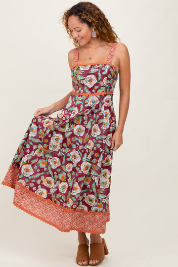 woman wearing a burgundy floral maxi dress with lace trim and spaghetti straps, posing with a smile