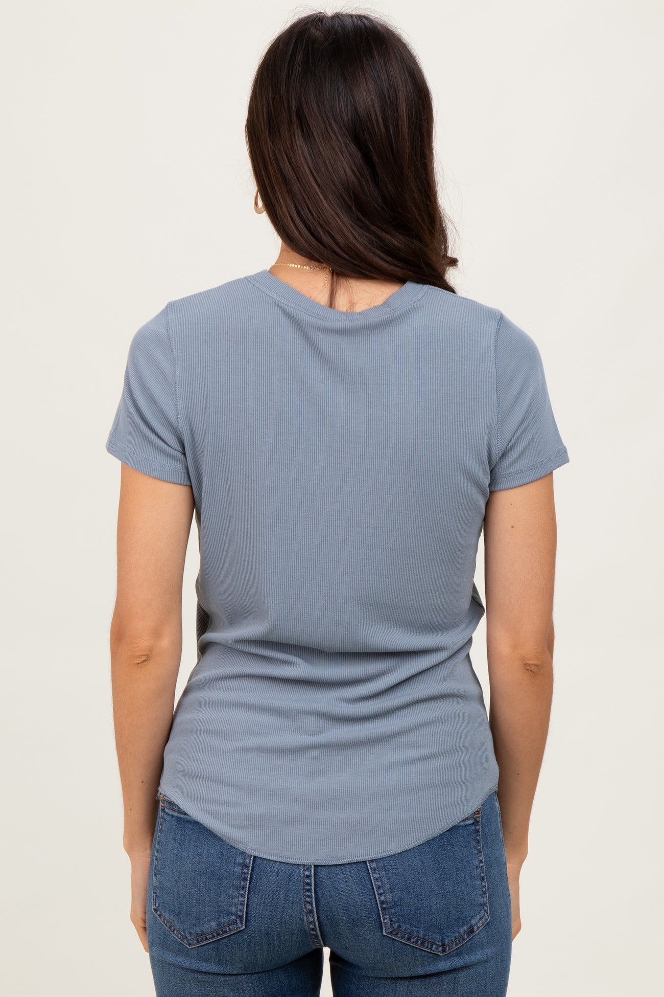 woman wearing a light blue ribbed short sleeve top and dark blue jeans, viewed from the back