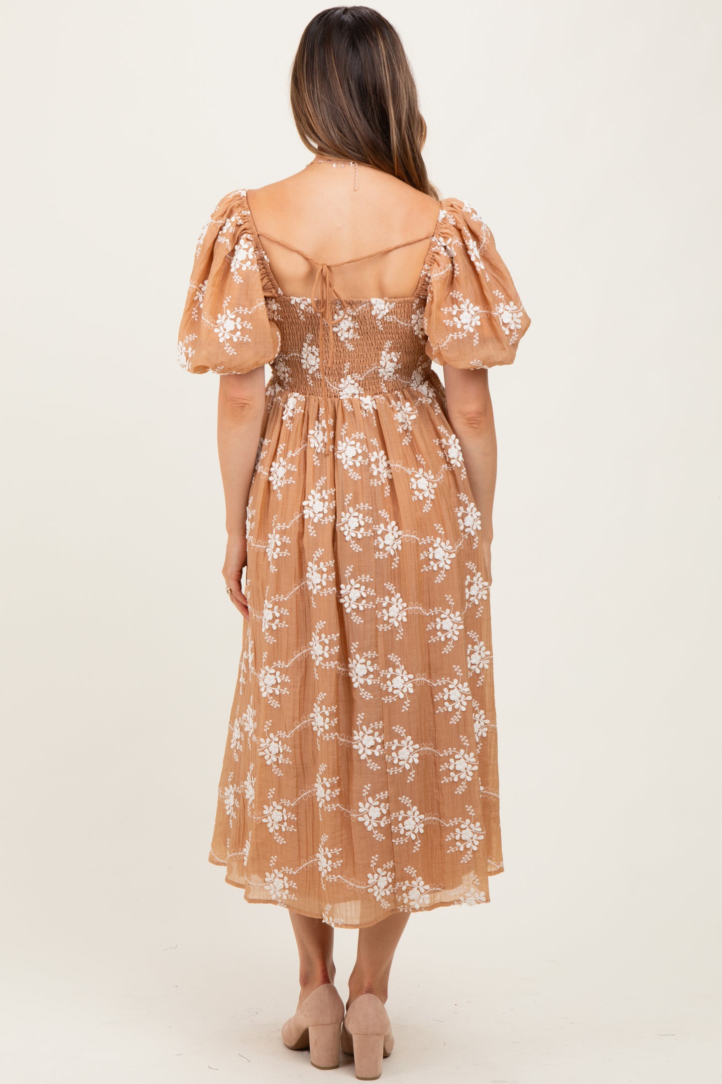 woman wearing a maternity floral midi dress with puff sleeves in a light brown shade, showing a smocked back detail