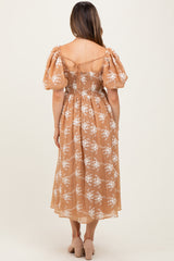woman wearing a maternity floral midi dress with puff sleeves in a light brown shade, showing a smocked back detail