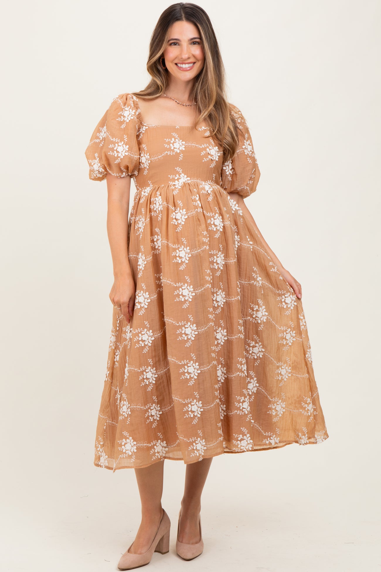 woman wearing a tan floral print maternity dress with puff sleeves and a flowing skirt