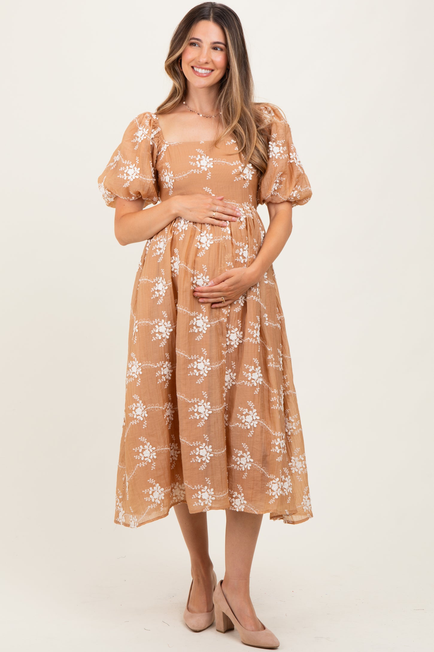woman wearing a tan floral maternity dress with puff sleeves and holding her baby bump