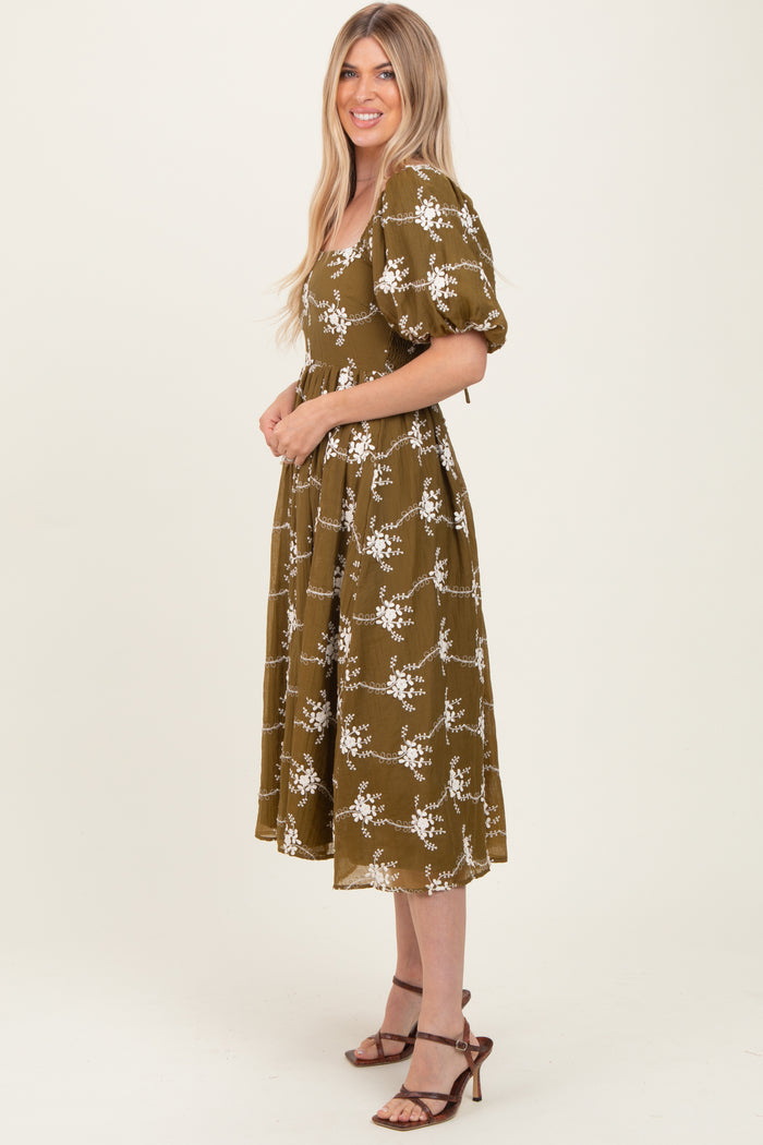woman wearing an olive green floral midi dress with puff sleeves and a square neckline, standing sideways