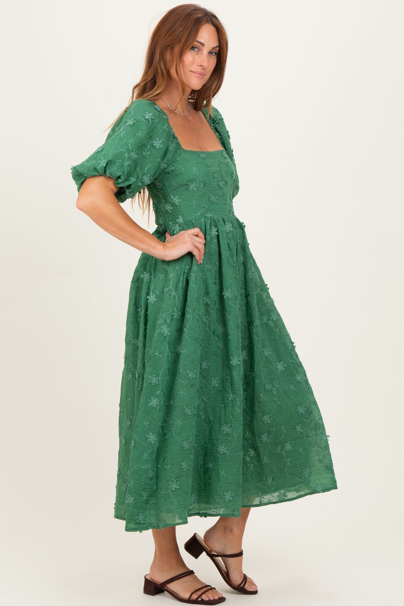 woman wearing a green midi dress with puff sleeves and floral embroidery, standing in profile