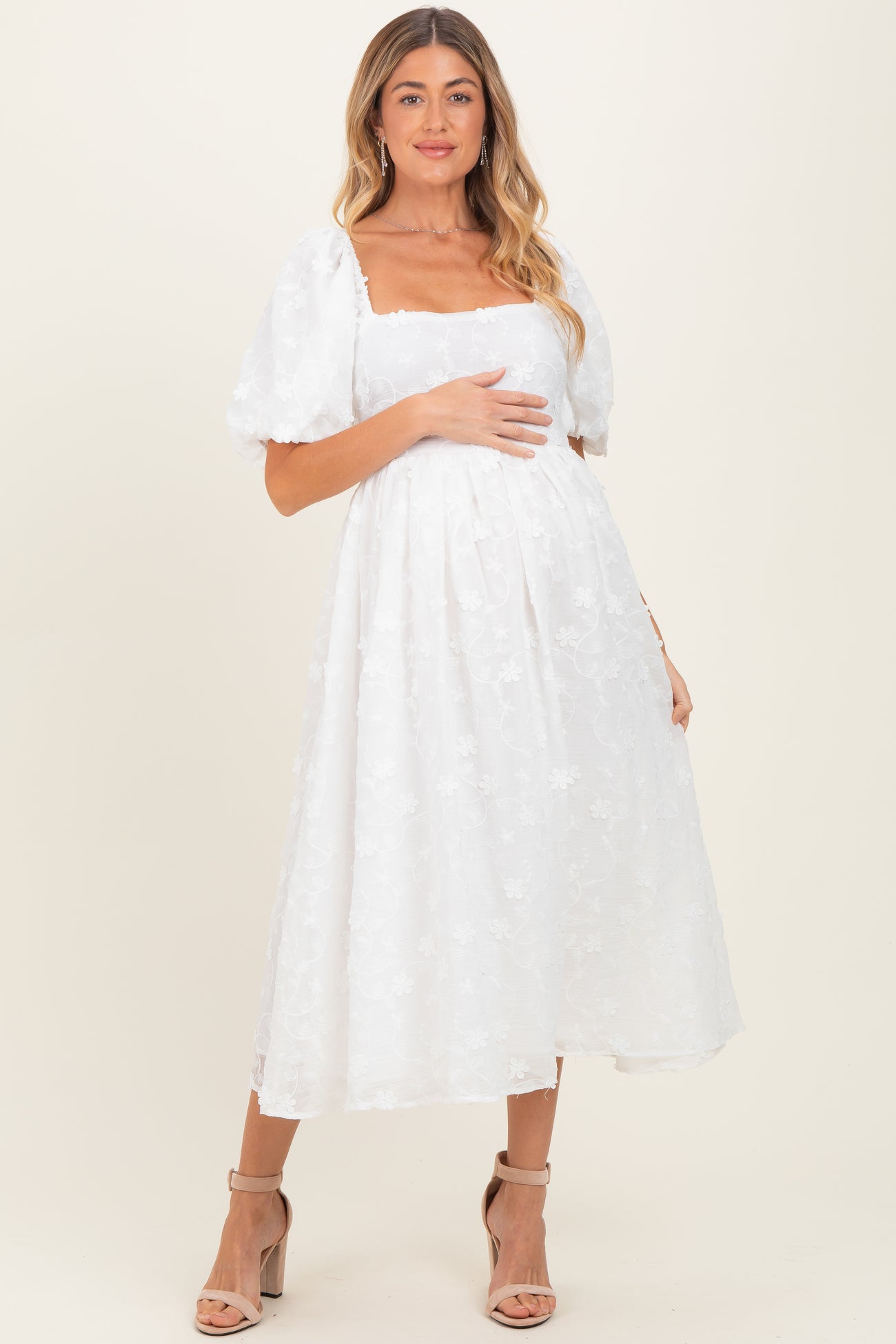 woman wearing a white floral maternity dress with puff sleeves and a fitted bodice, gently holding her baby bump