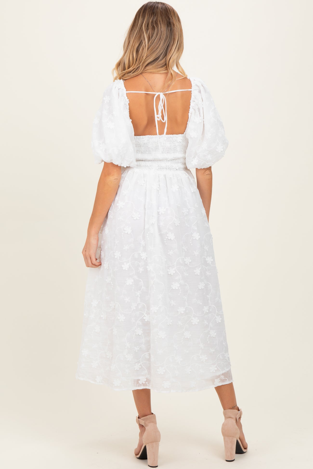 woman wearing a white puff sleeve maternity dress with floral embroidery and a smocked back detail