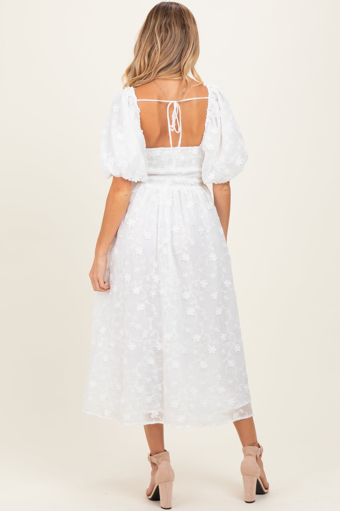 woman wearing a white puff sleeve maternity dress with floral embroidery and a smocked back detail