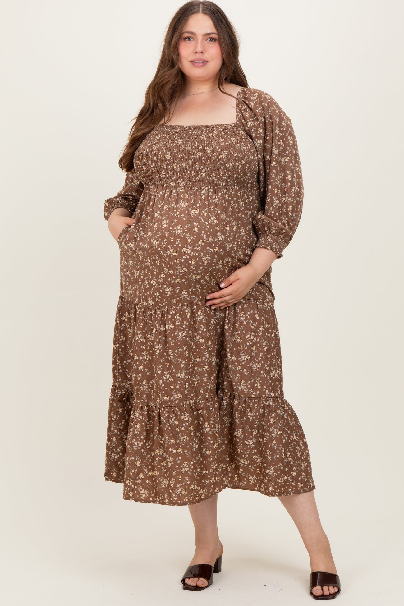 woman wearing a brown floral maternity wear maxi dress with puff sleeves and pockets, cradling her baby bump