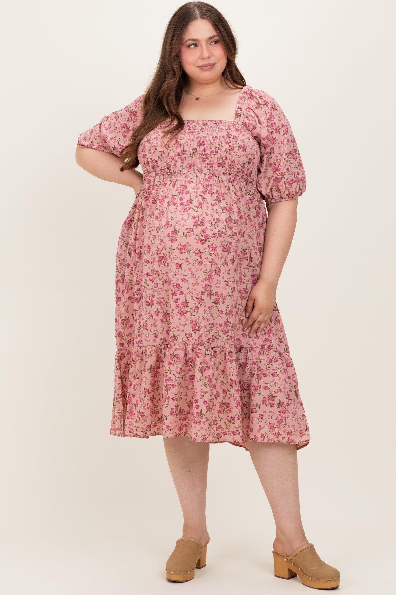 woman wearing a pink floral maternity dress with puff sleeves and ruffle hem, showing her baby bump