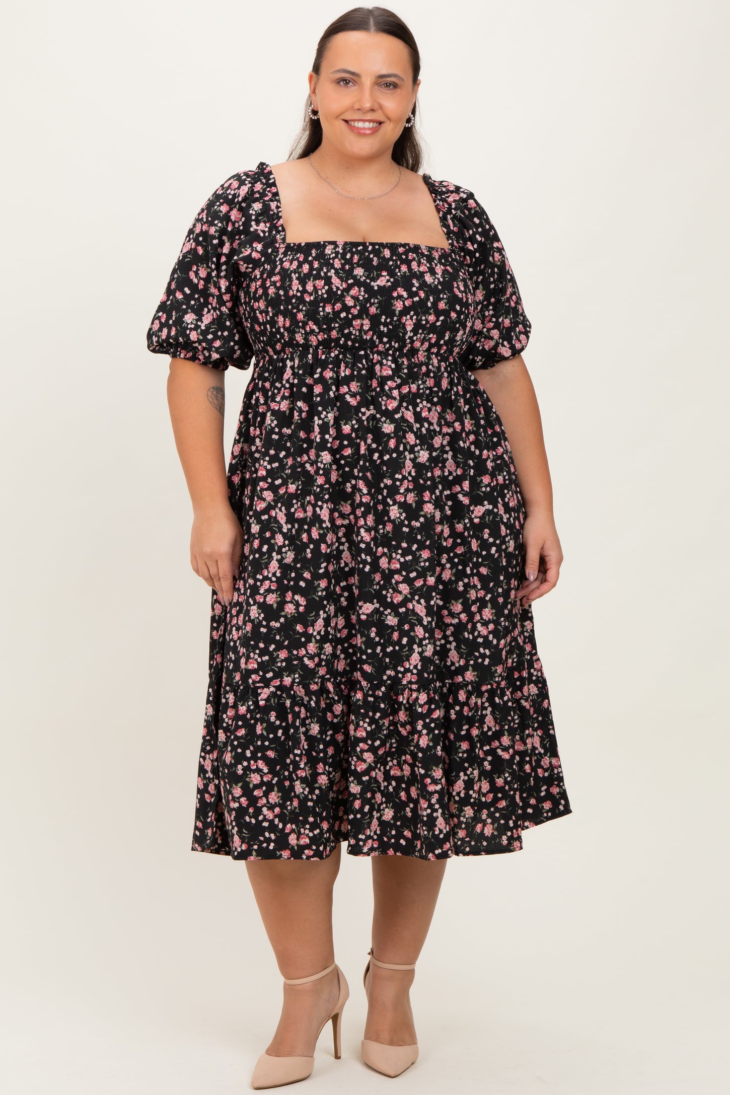 woman wearing a black floral plus size dress with puff sleeves and a tiered skirt, standing in neutral background