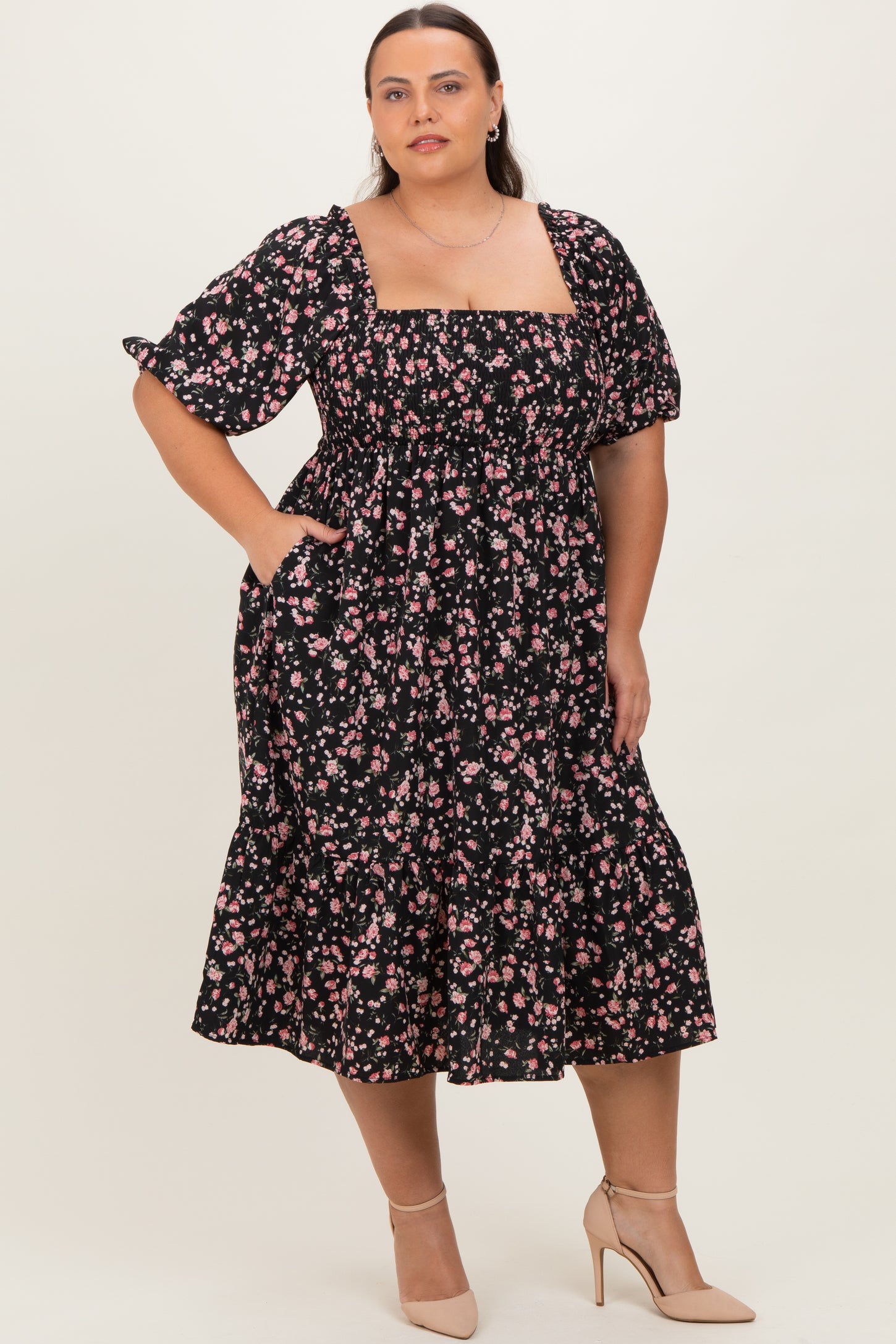 woman wearing a black floral plus size midi dress with puff sleeves and pockets, standing in a neutral background
