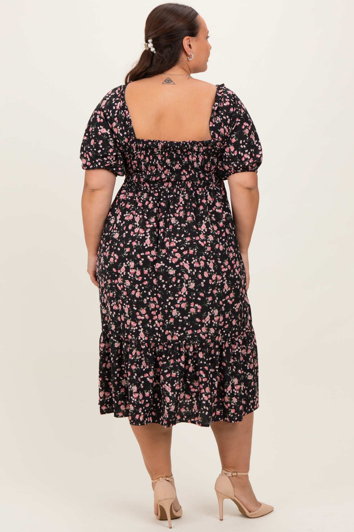 woman wearing a black floral plus-size dress with puff sleeves and a tiered hem, viewed from the back
