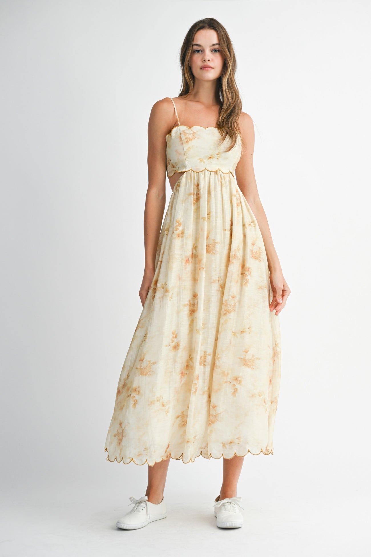 woman wearing a light yellow floral maxi dress with spaghetti straps and scalloped edges