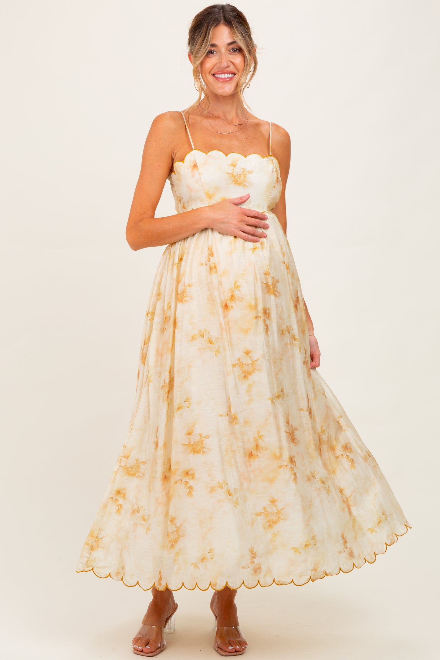 woman wearing a floral maternity maxi dress with scalloped detailing and holding her baby bump