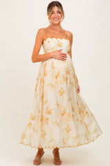 woman wearing a floral maternity maxi dress with scalloped detailing and holding her baby bump