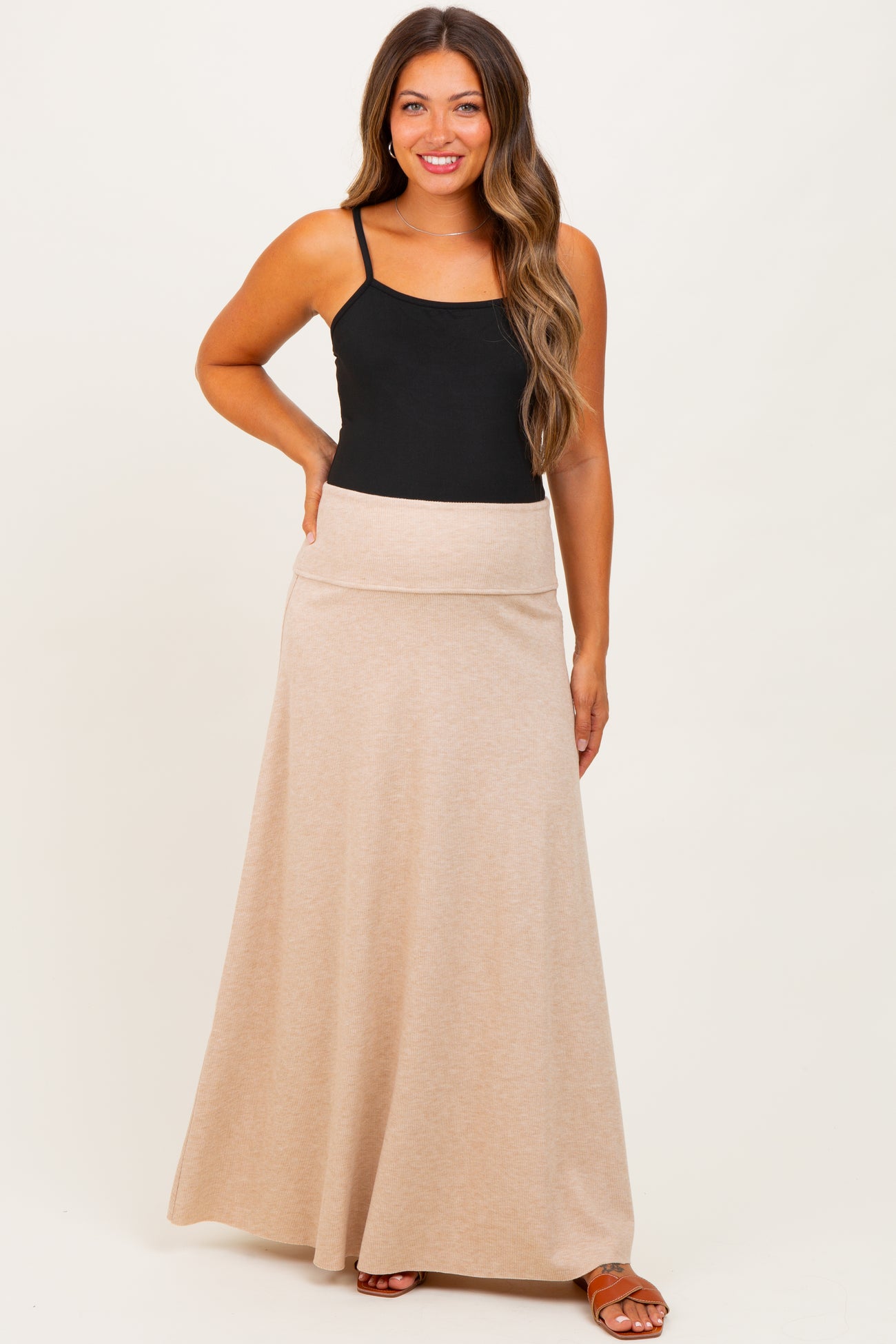 woman wearing a black tank top and a beige maternity maxi skirt with a comfortable waistband and posing with a smile