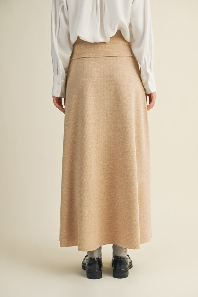 woman wearing a beige long maxi skirt and a white button-up shirt, viewed from the back