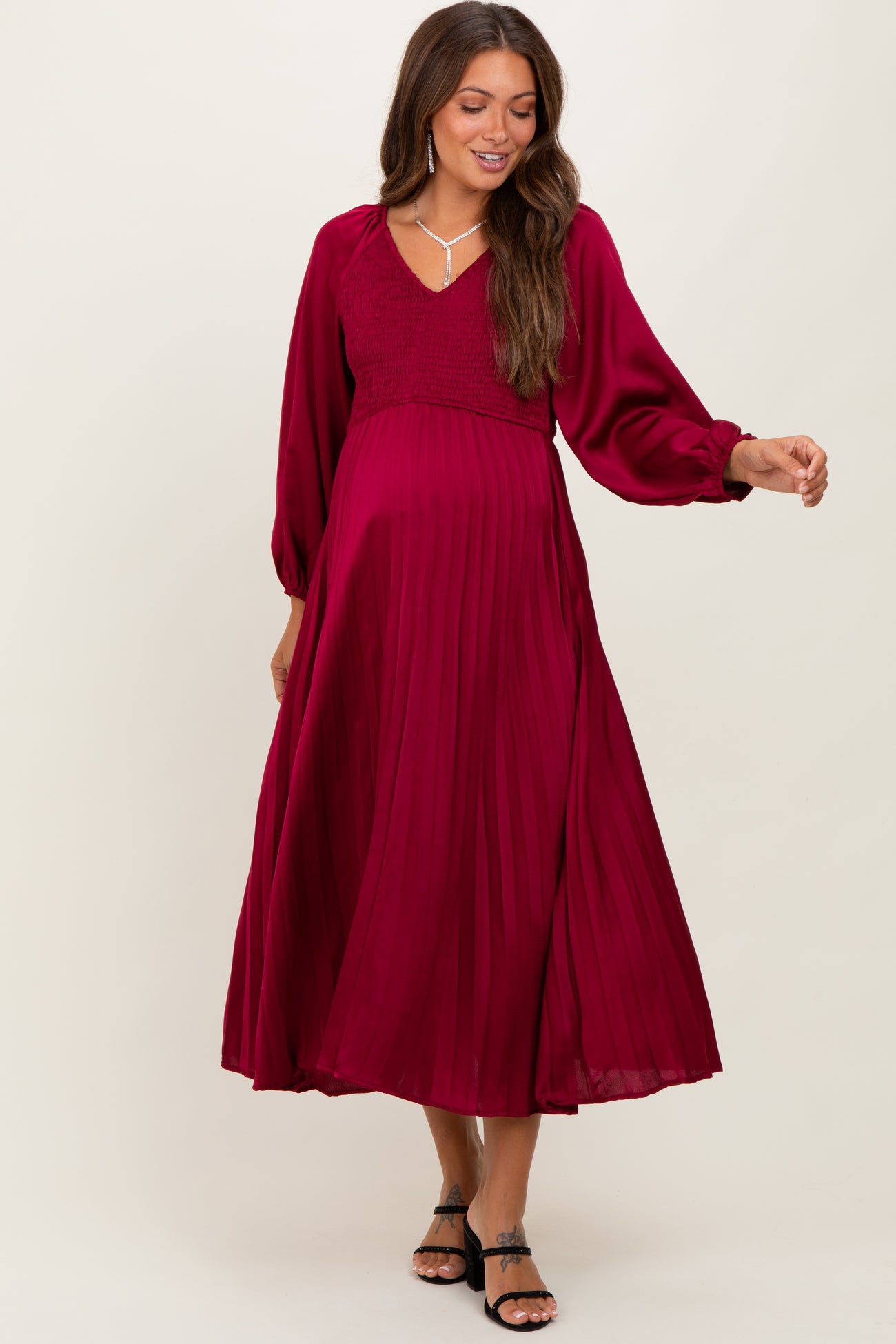 woman wearing a burgundy maternity dress with a smocked bodice and pleated skirt, showcasing her baby bump