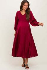 woman wearing a burgundy maternity dress with a smocked bodice and pleated skirt, showcasing her baby bump
