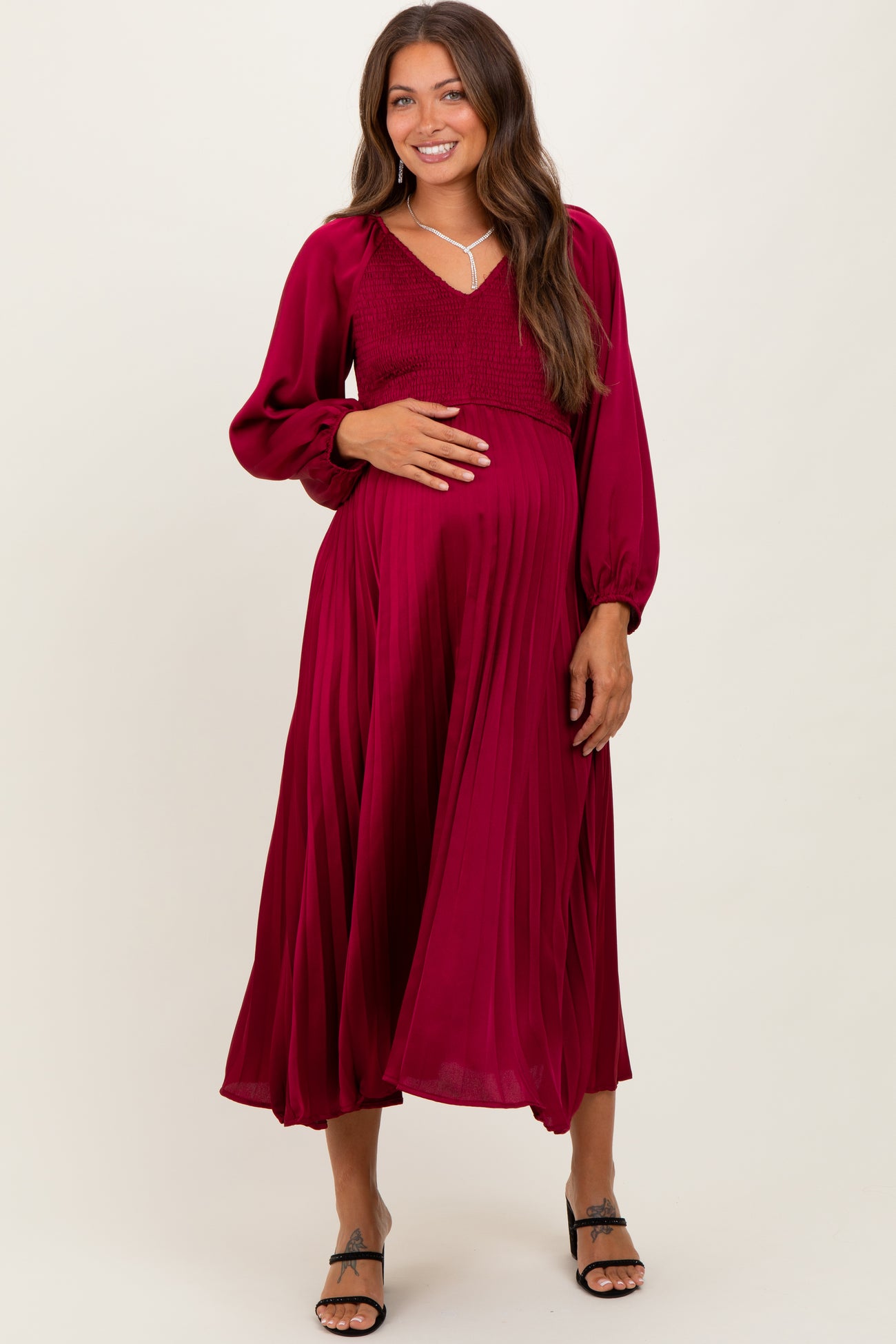 woman wearing a burgundy maternity maxi dress with long sleeves and smocked bodice, holding her baby bump