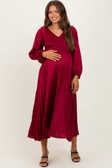 woman wearing a burgundy maternity maxi dress with long sleeves and smocked bodice, holding her baby bump