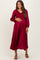 woman wearing a burgundy maternity maxi dress with long sleeves and smocked bodice, holding her baby bump