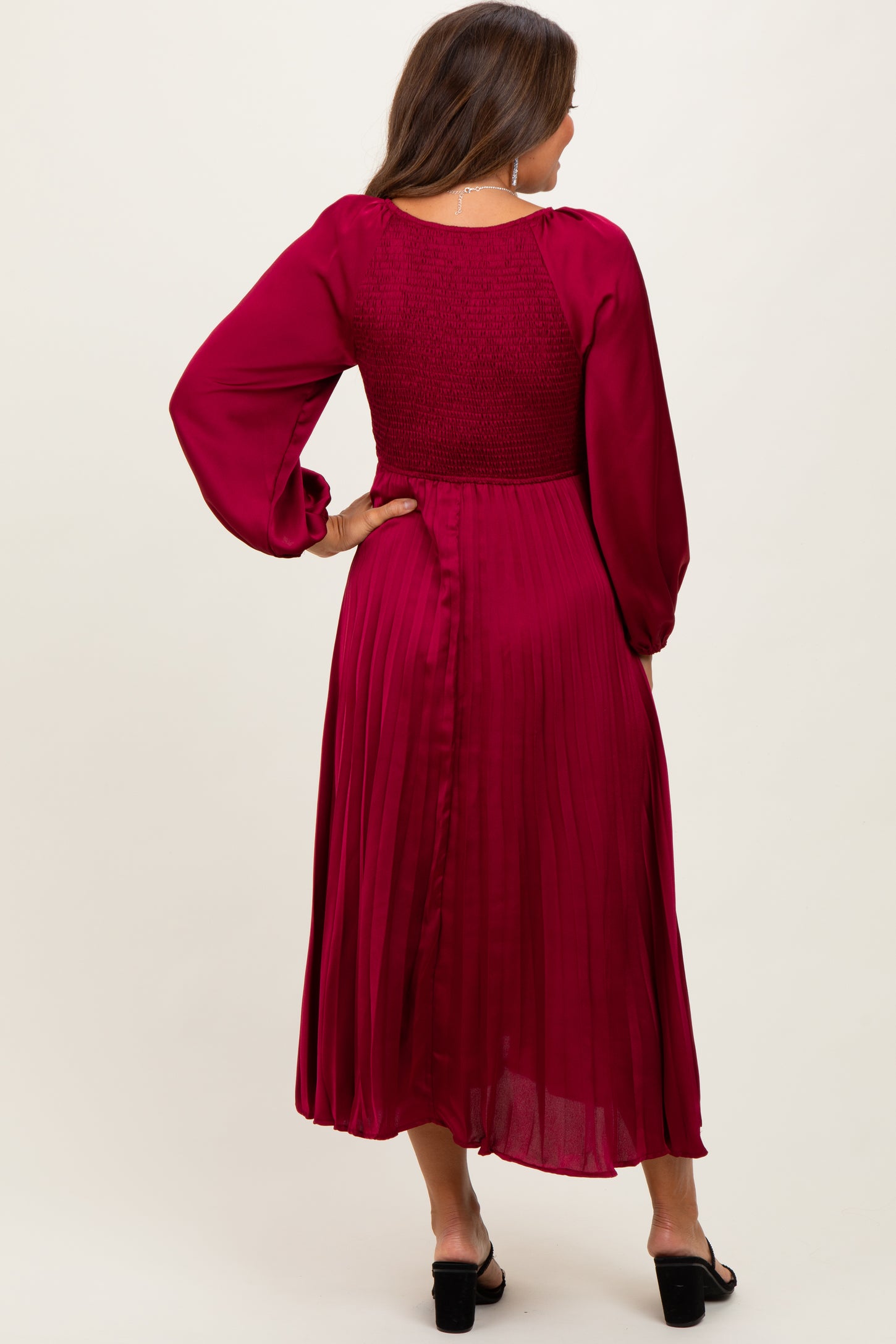 woman wearing a deep burgundy maternity dress with a pleated skirt and smocked bodice, featuring long sleeves