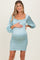 woman wearing a light blue maternity dress with ruffled neckline and puff sleeves, showcasing her baby bump