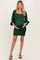 woman wearing a green maternity dress with a smocked body and long satin sleeves, holding her baby bump