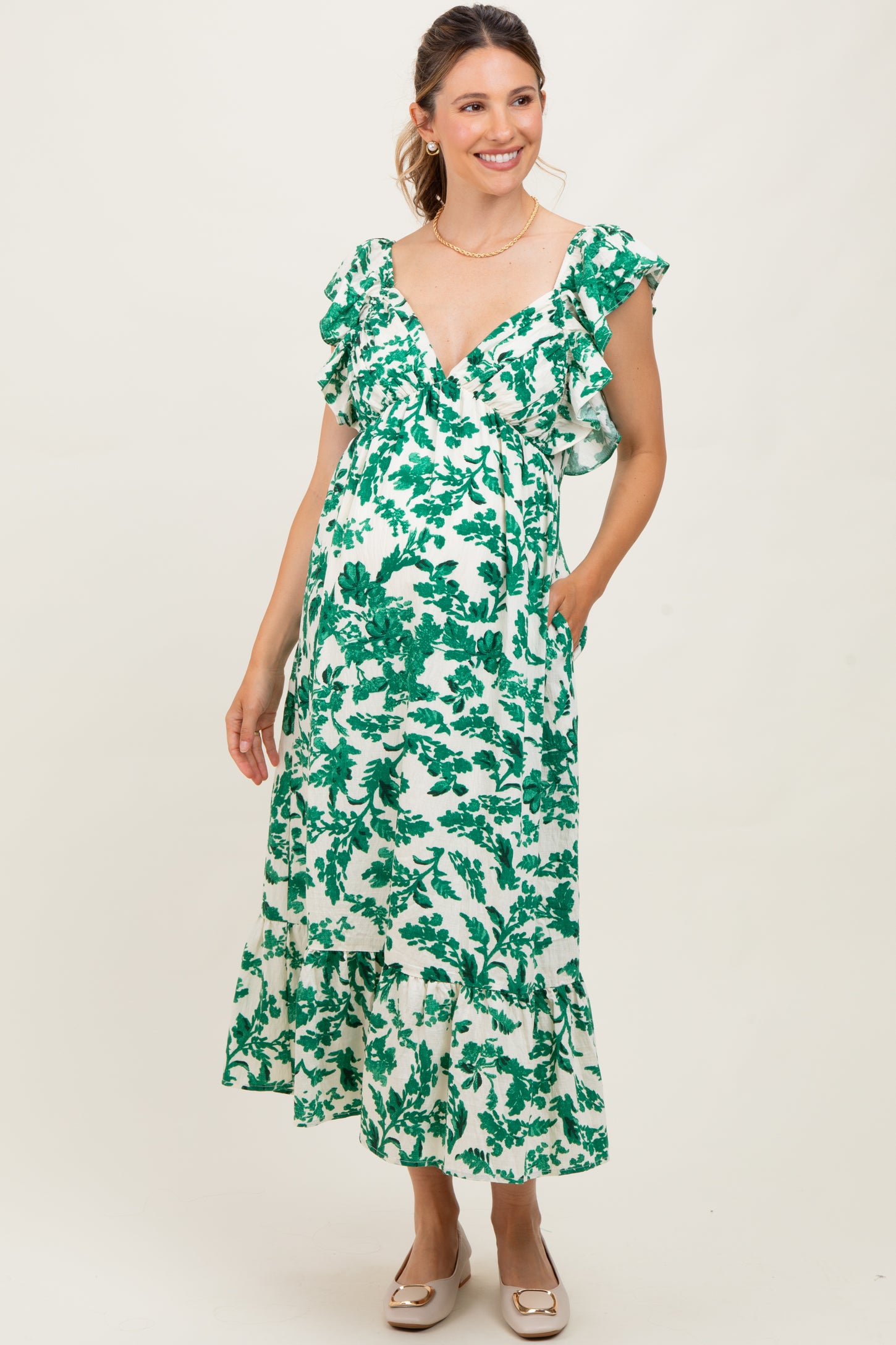 woman wearing a green floral maternity dress with ruffled sleeves and a tiered hem, showing her baby bump