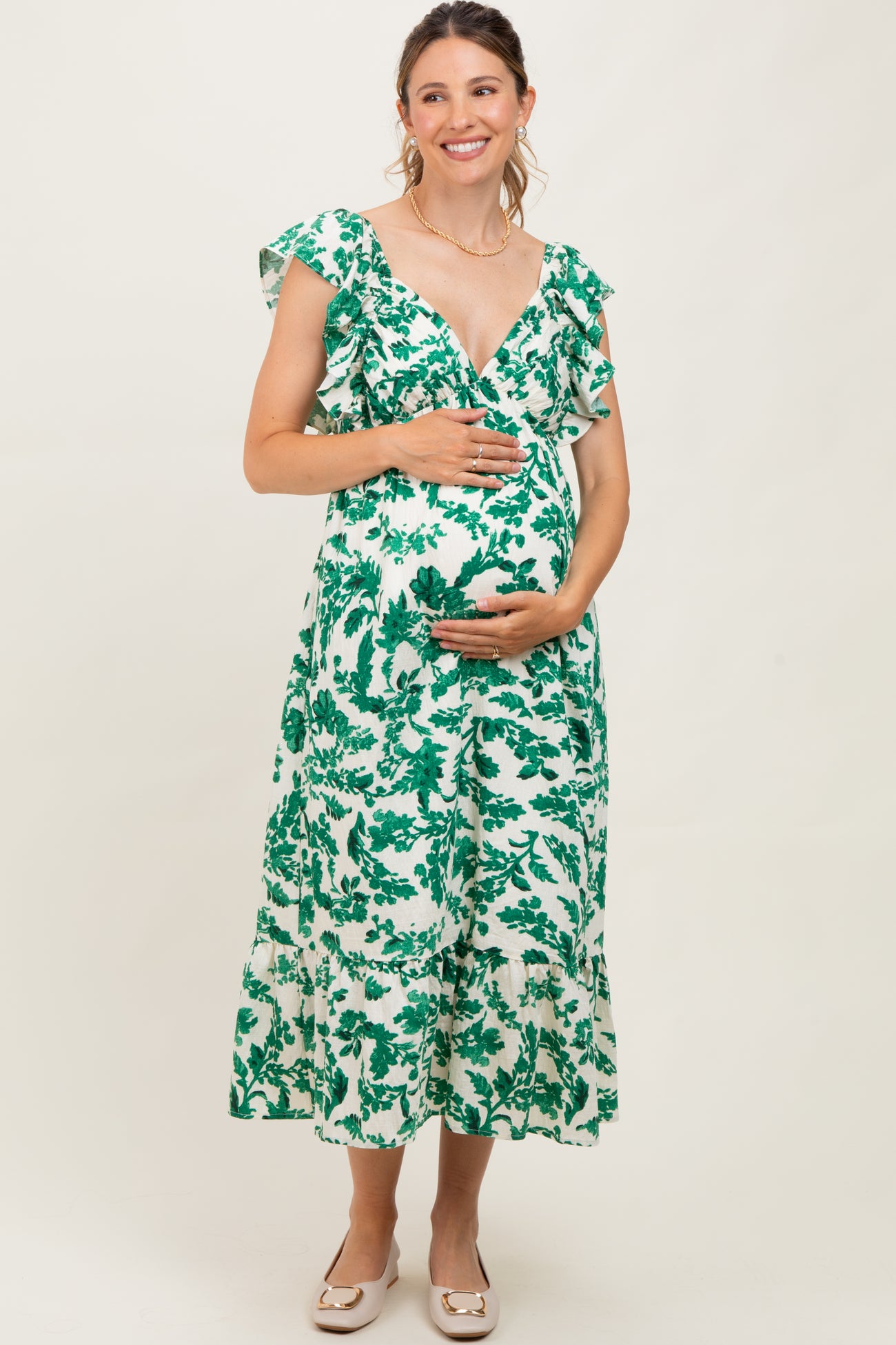 woman wearing a green and white floral maternity dress with ruffled sleeves and a baby bump
