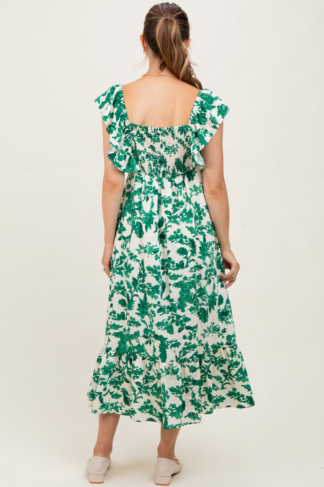 woman wearing a green floral print maternity maxi dress with ruffled sleeves and smocked back detail