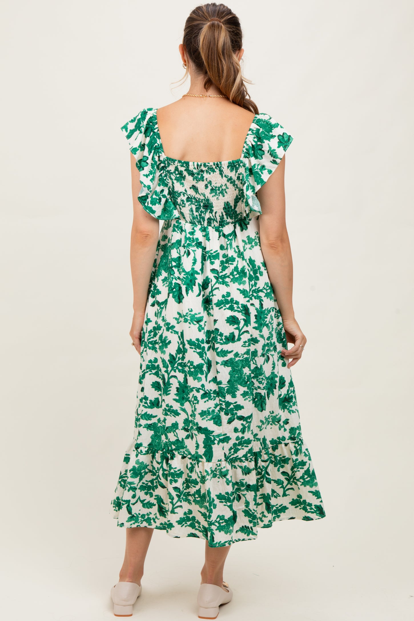 woman wearing a green floral print maternity maxi dress with ruffled sleeves and smocked back detail