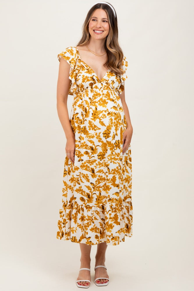 woman wearing a floral print yellow and white maternity dress with ruffle sleeves and a tiered skirt, showing her baby bump