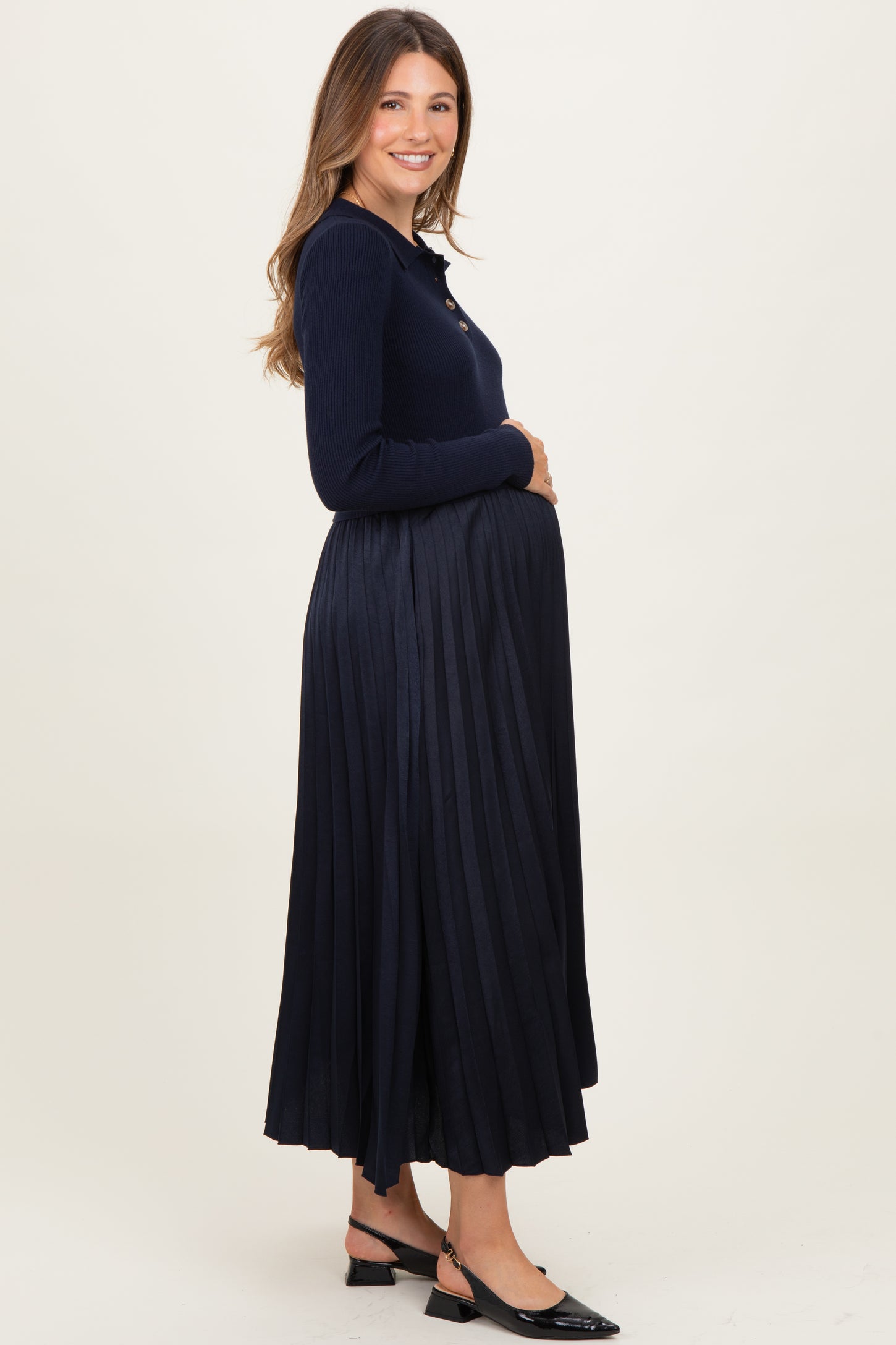 woman wearing a navy blue maternity sweater and a pleated maxi skirt, showing her baby bump