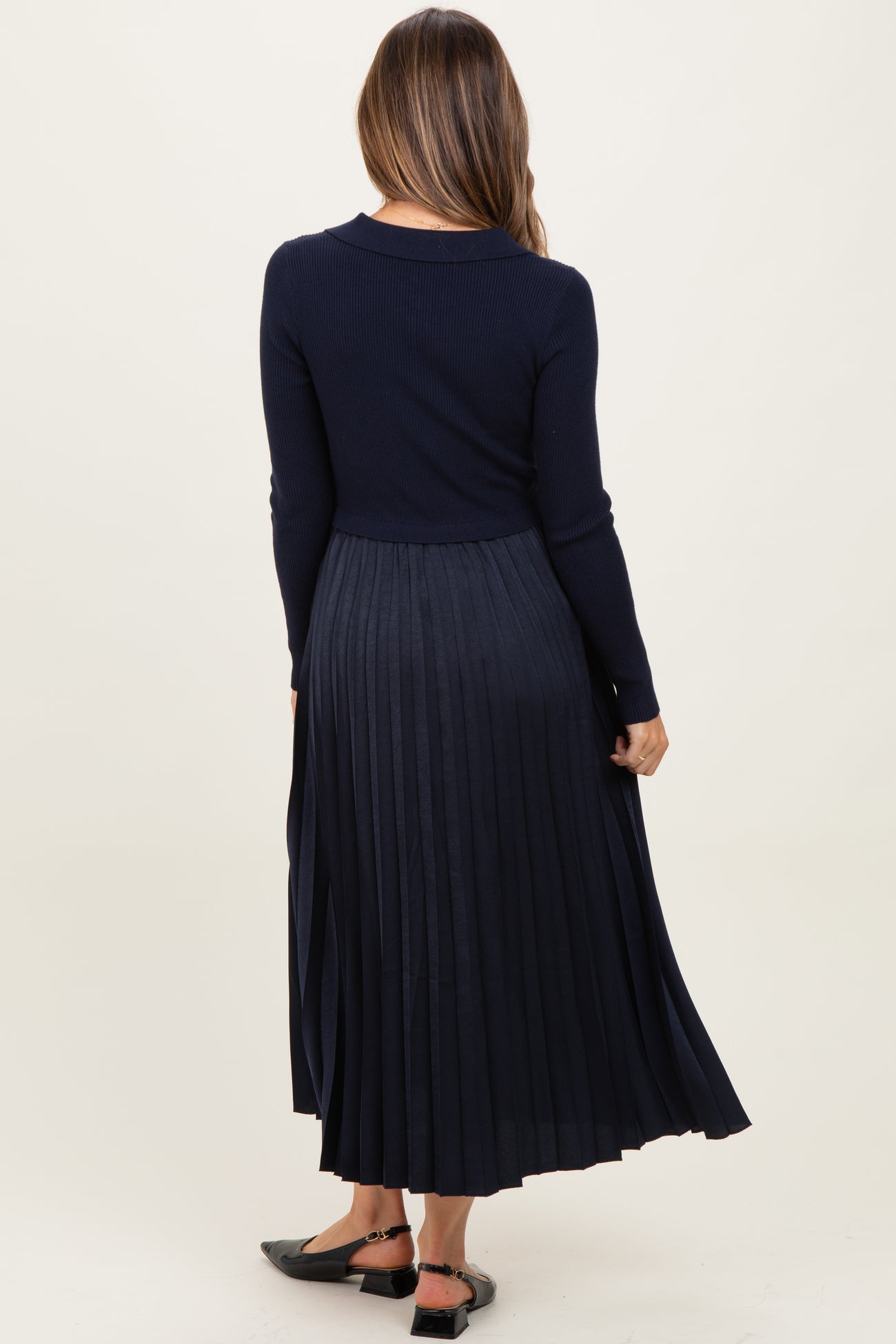 woman wearing a navy blue long sleeve maternity dress with a pleated skirt, showing her back and no visible baby bump