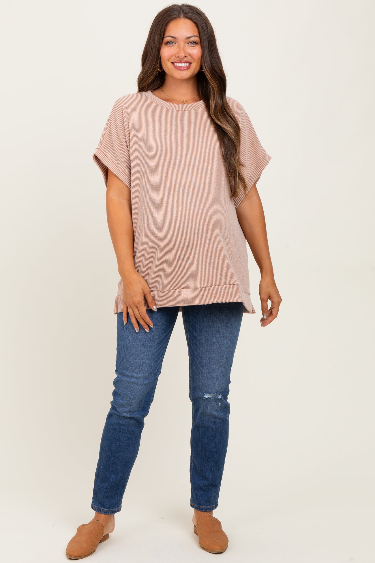 woman wearing a blush ribbed maternity top and blue distressed skinny jeans, showcasing her baby bump
