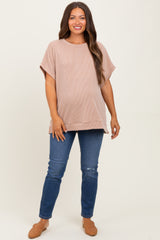woman wearing a blush ribbed maternity top and blue distressed skinny jeans, showcasing her baby bump