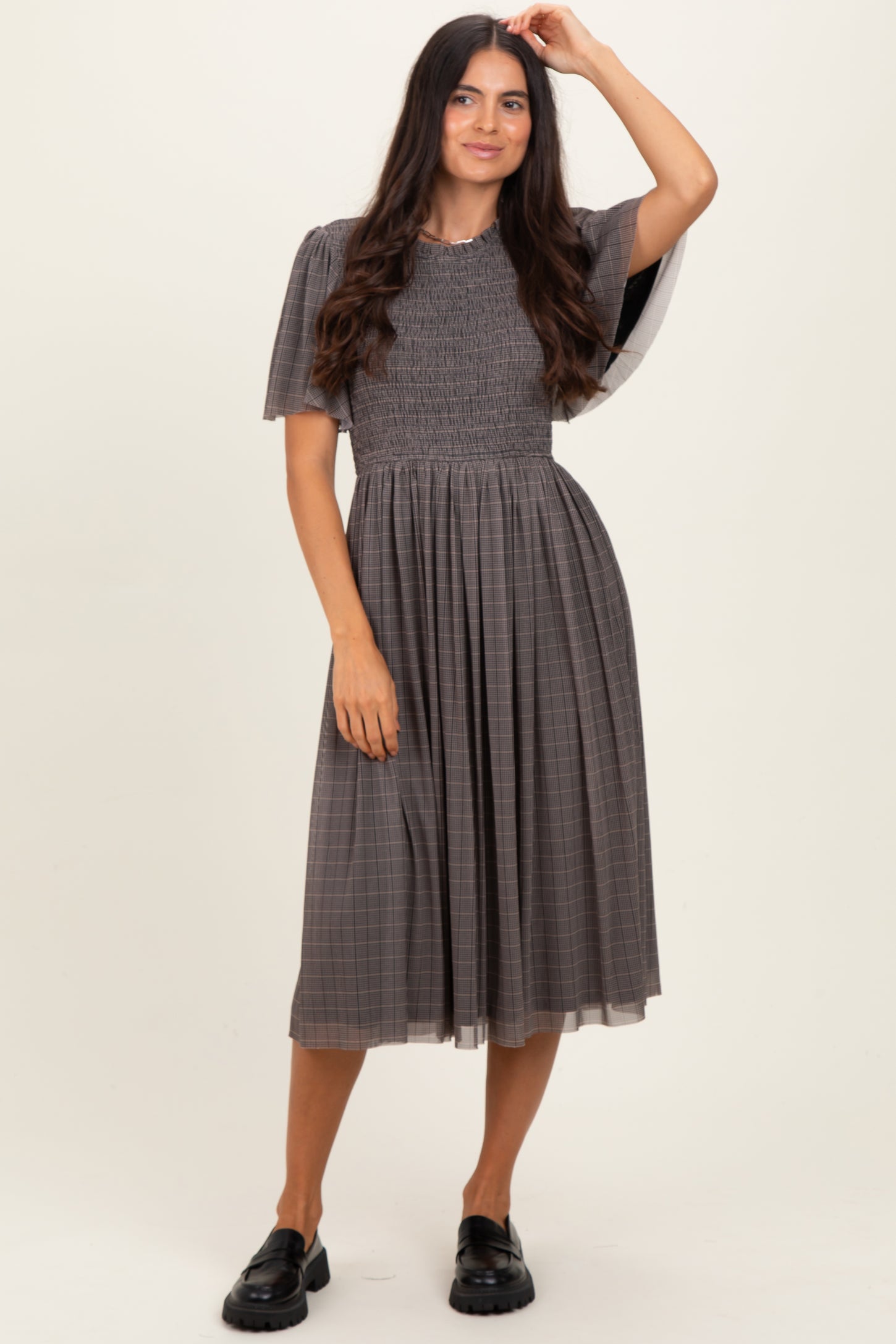 woman wearing a grey plaid midi dress with smocked bodice and puff sleeves, styled with black chunky loafers