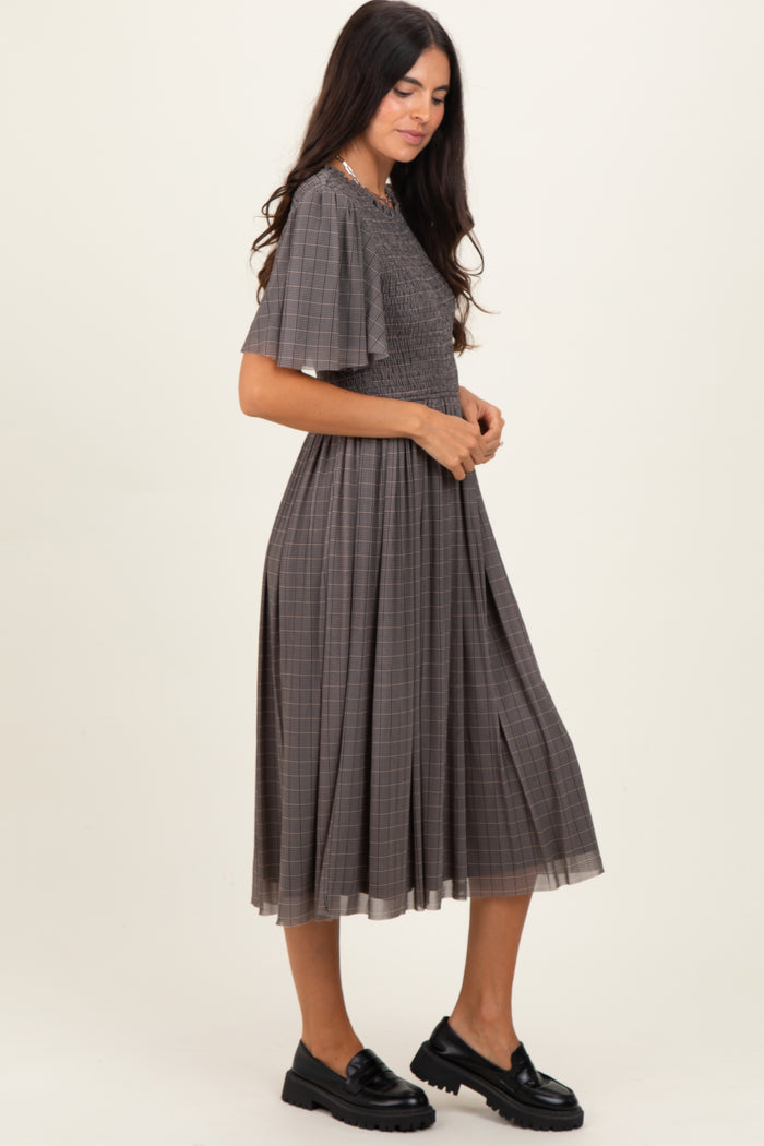 woman wearing a gray checkered midi dress with short flutter sleeves and pleated skirt, styled with black loafers