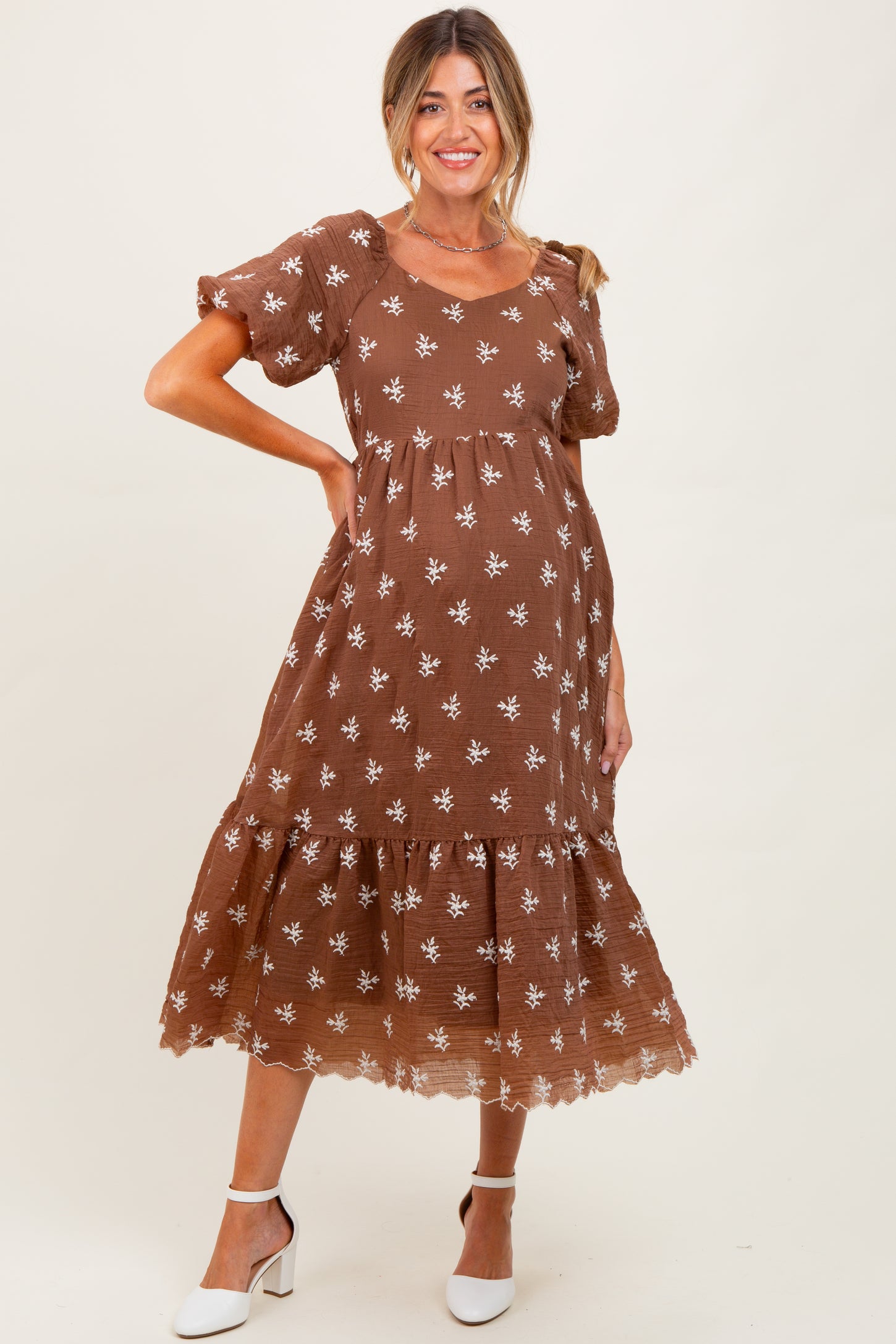 woman wearing a brown floral maternity dress with puff sleeves and a tiered skirt, showcasing a baby bump