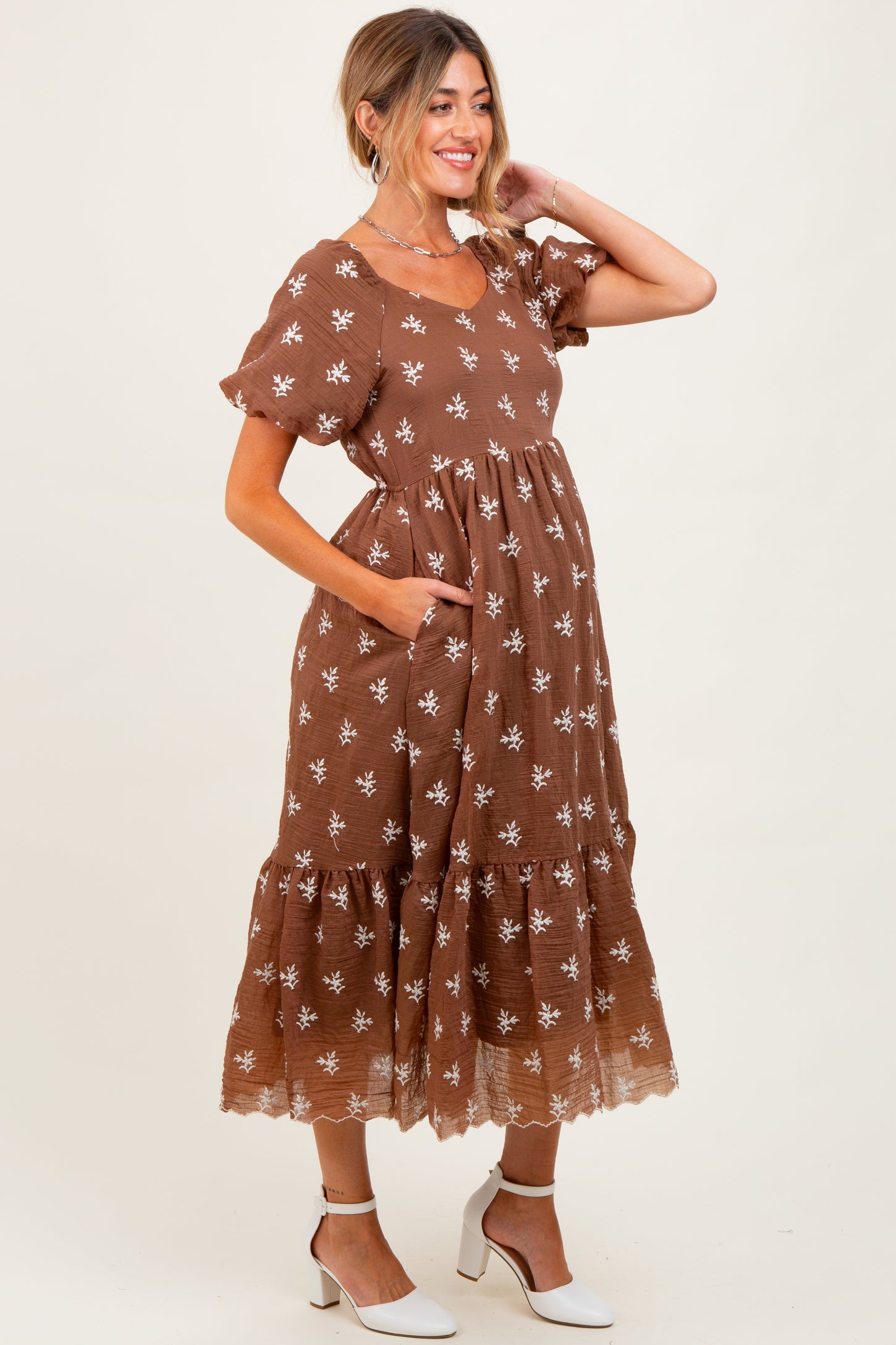 woman wearing a brown floral maternity dress with short sleeves and pockets, showcasing a baby bump