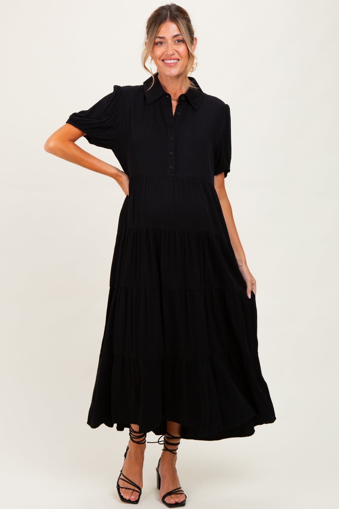 woman wearing a black tiered button-up maternity dress with short puff sleeves and a visible baby bump