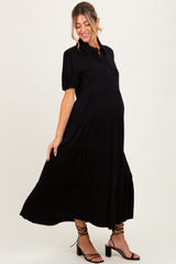 woman wearing a black maternity maxi dress with puff sleeves and a tiered skirt, showcasing her baby bump