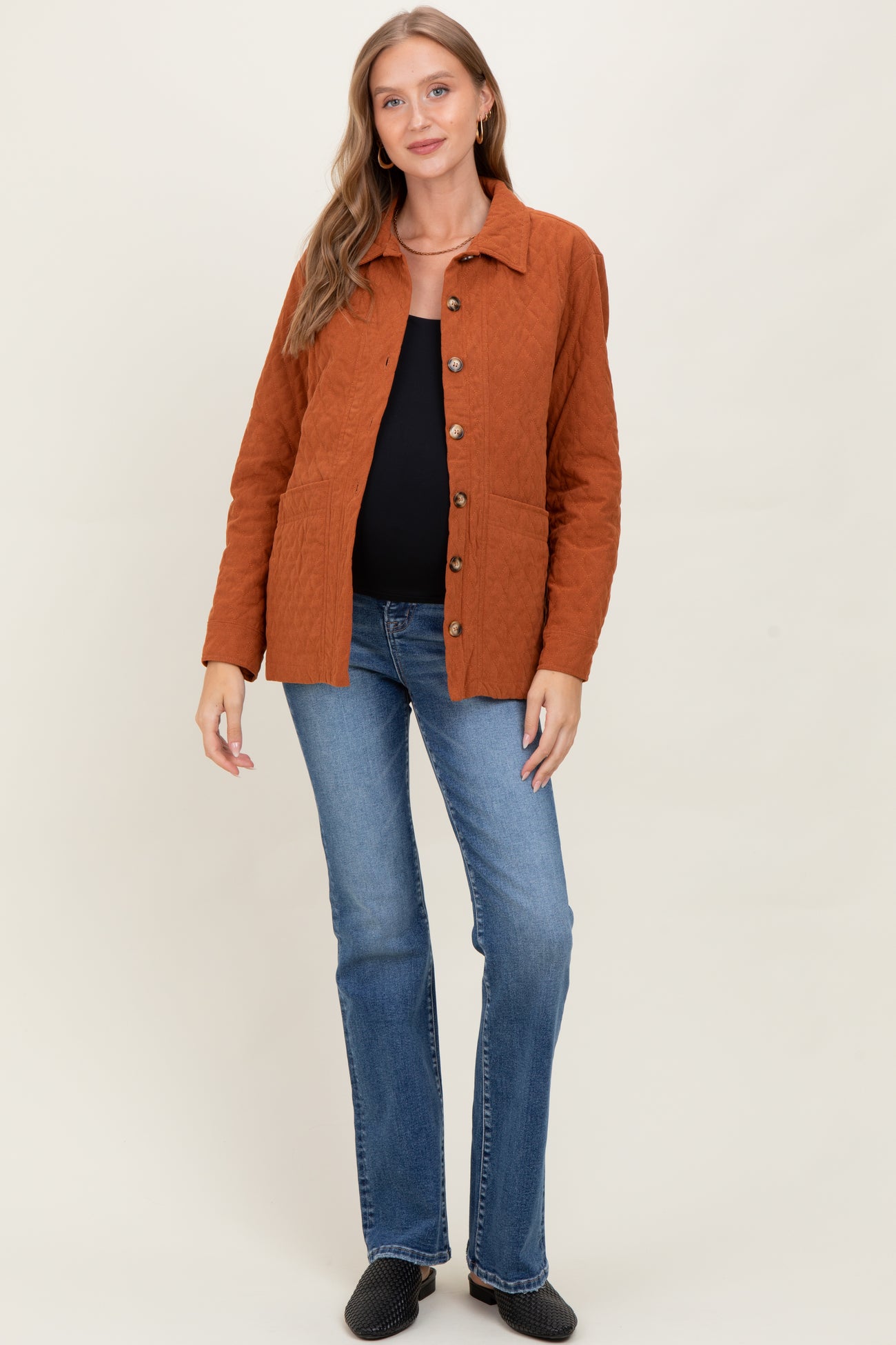 woman wearing a rust-colored maternity jacket over a black top paired with blue flared jeans