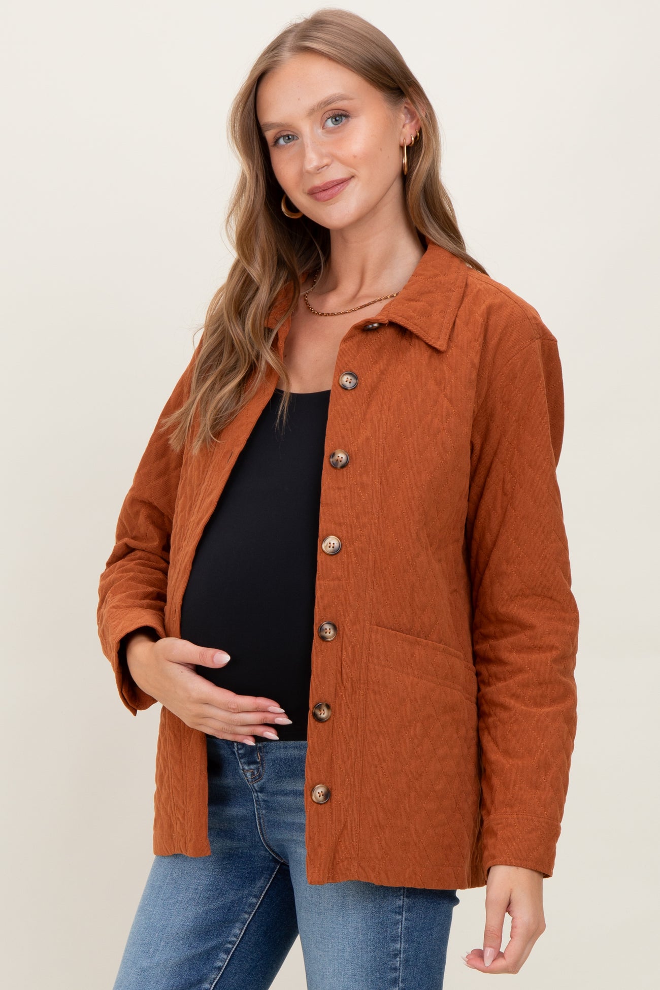 woman wearing a rust quilted maternity jacket over a black top, gently holding her baby bump